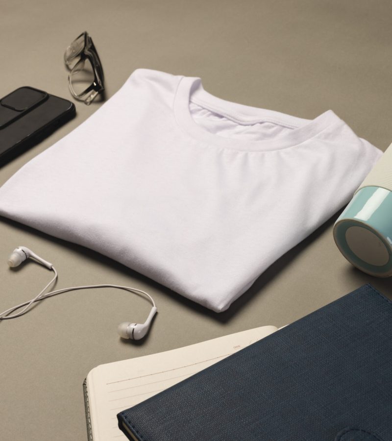 Flat lay of white t shirt, smartphone, earphones and notebooks with copy space on grey background. Fashion, clothes, colour and fabric concept.